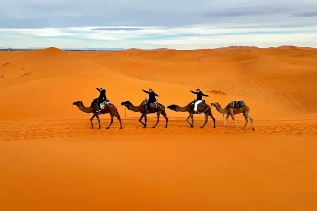Viajeros en fila sobre dromedarios avanzando por las dunas de Erg Chebbi, en Merzouga, a la hora del atardecer